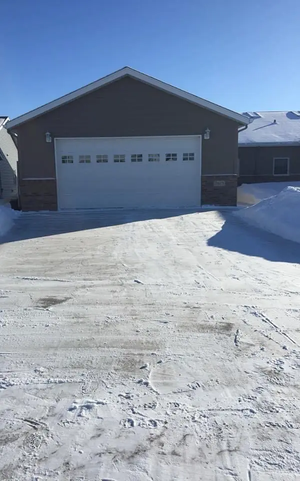 Driveway cleared down to the pavement in front of a two-stall garage after a snowfall