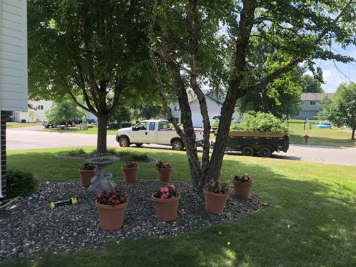 Rock bed with flower pots under a tree, Mow Me truck and trailer at the curb
