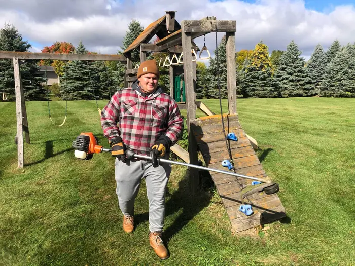 Crew member with a string trimmer next to a backyard play set