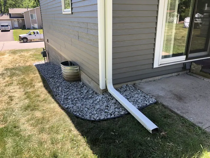 White rock bed with a downspout along gray siding